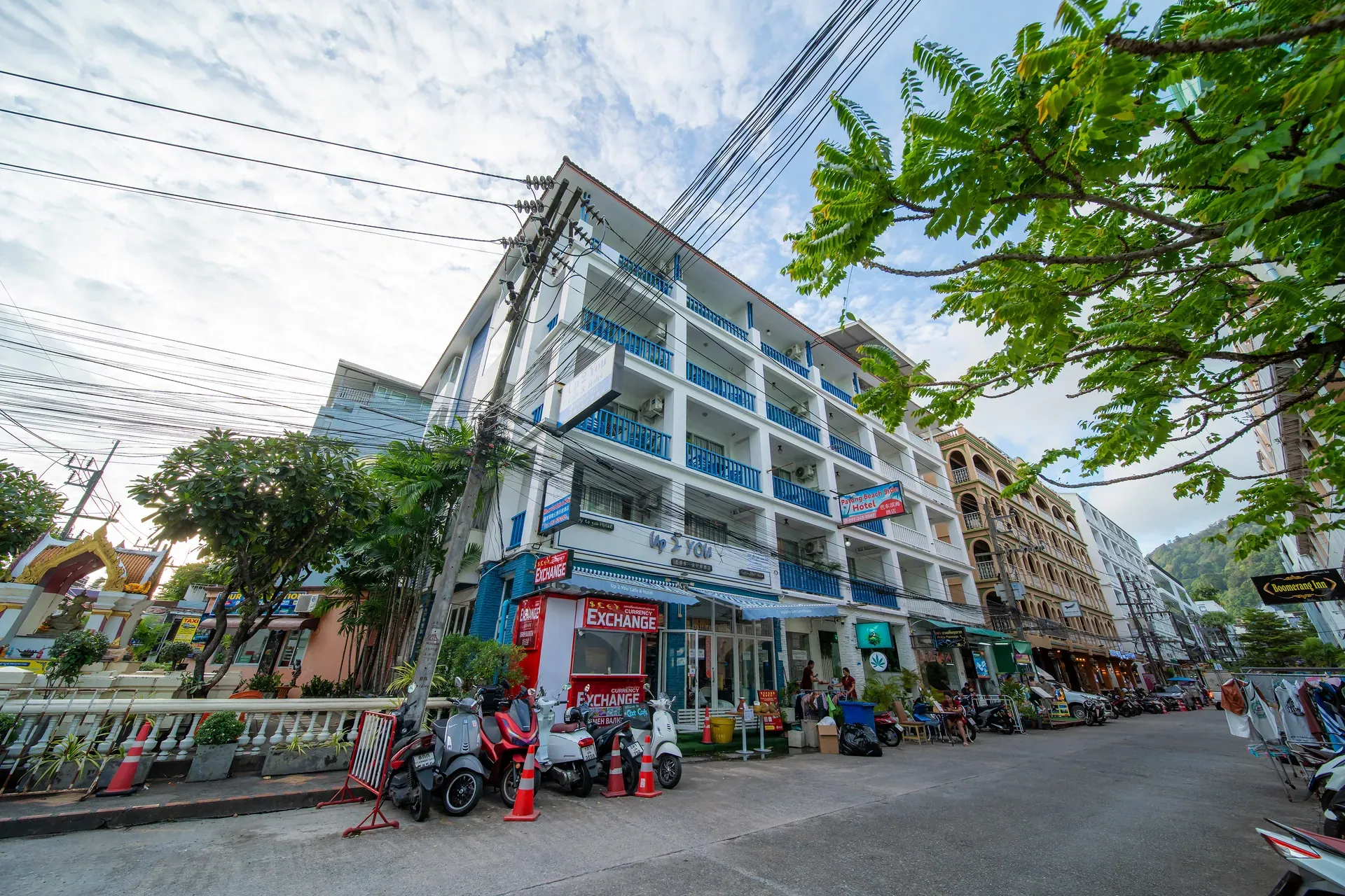The hotel building on a Patong street, with blue balcony railings above ground-floor shops