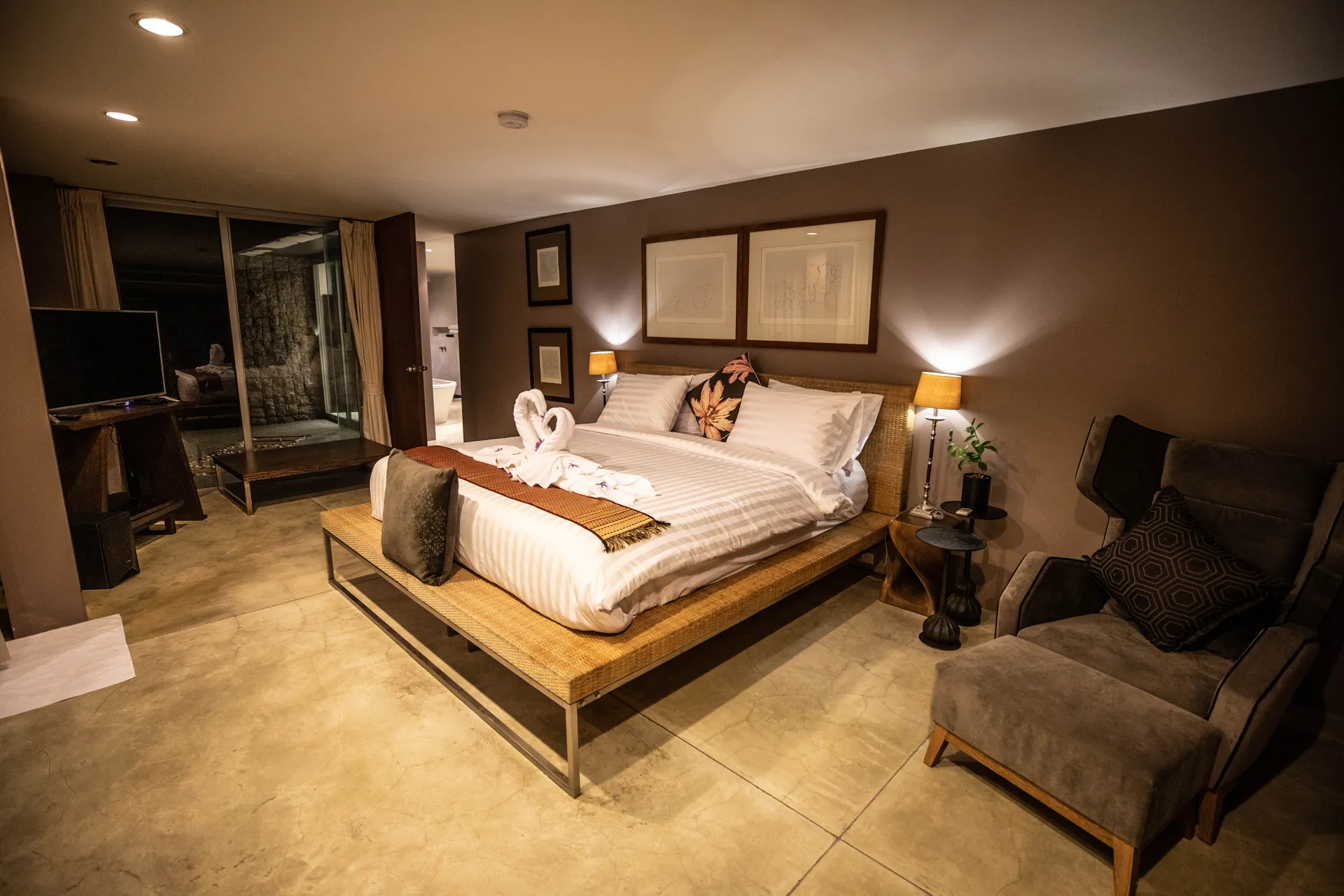 Bedroom in warm brown tones with a platform bed, reading lamps and an armchair