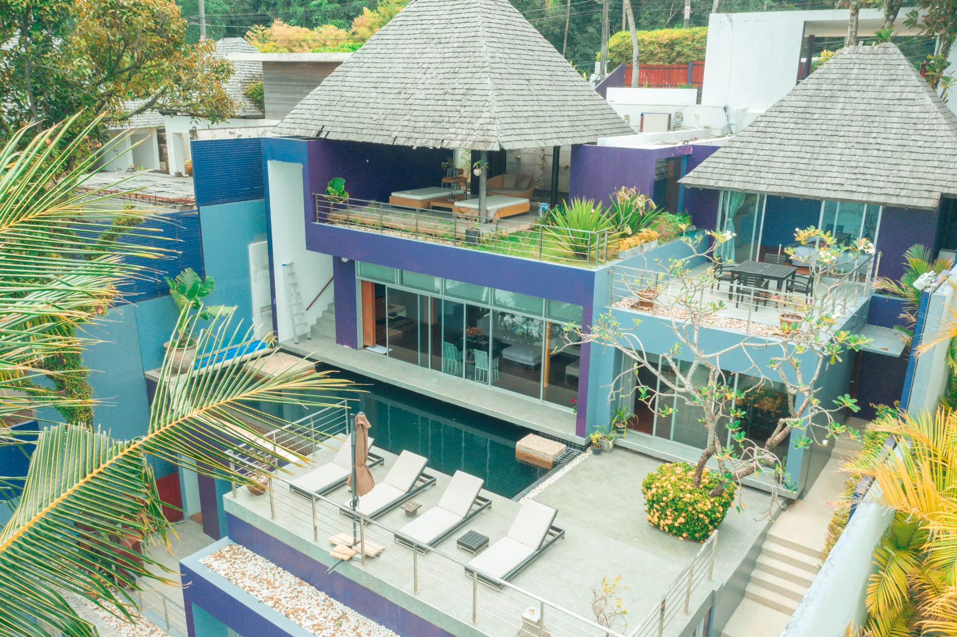 Aerial view of the villa's terraces, pool and thatched rooftop sala among palm trees