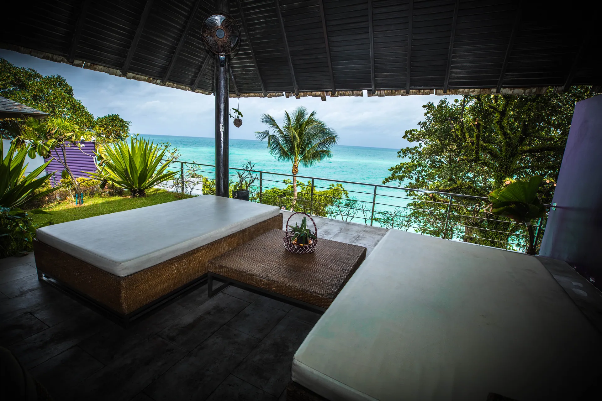 Covered sala with cushioned daybeds, open to the garden and the sea