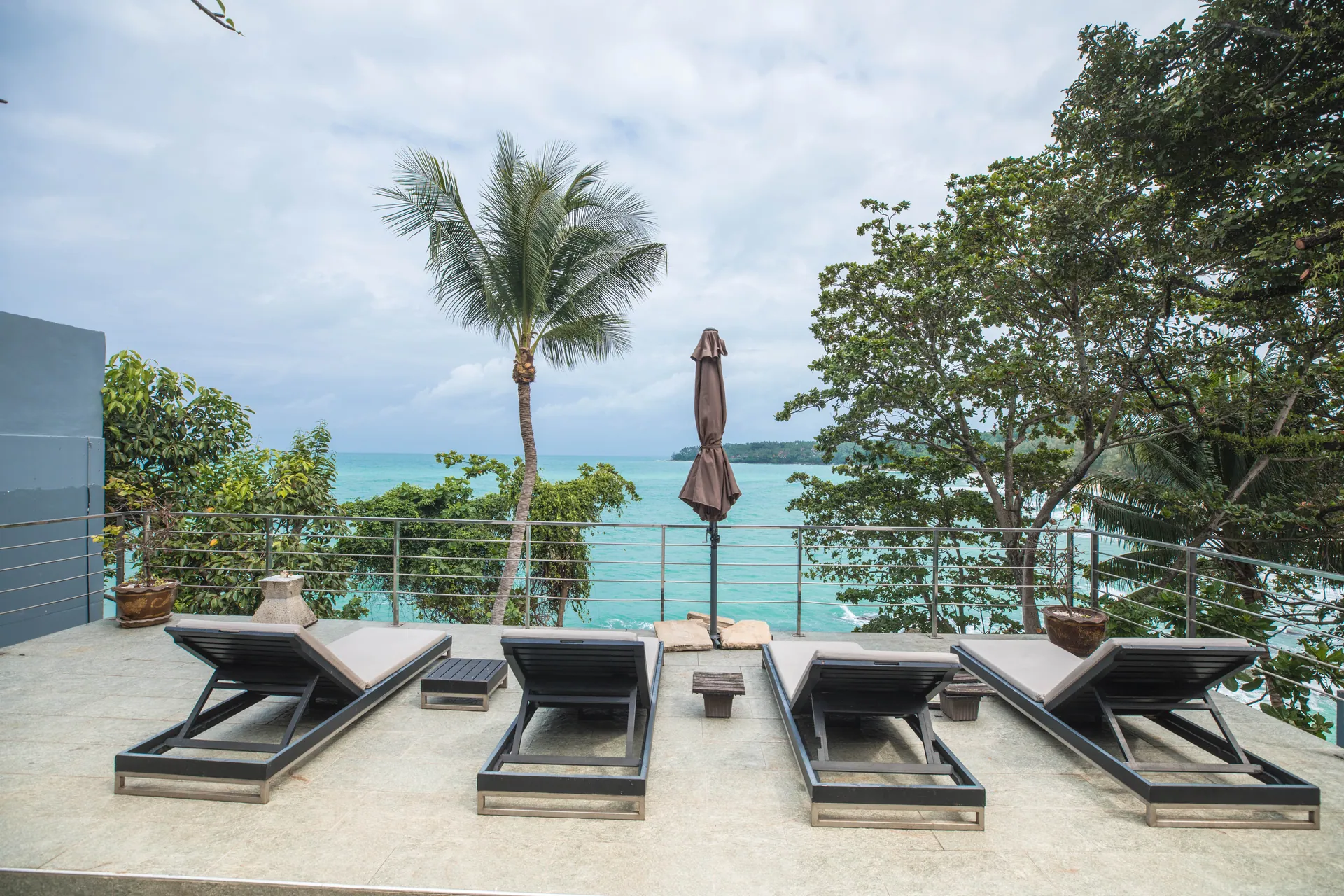 Four sun loungers on a railed terrace looking out to the sea and a distant headland