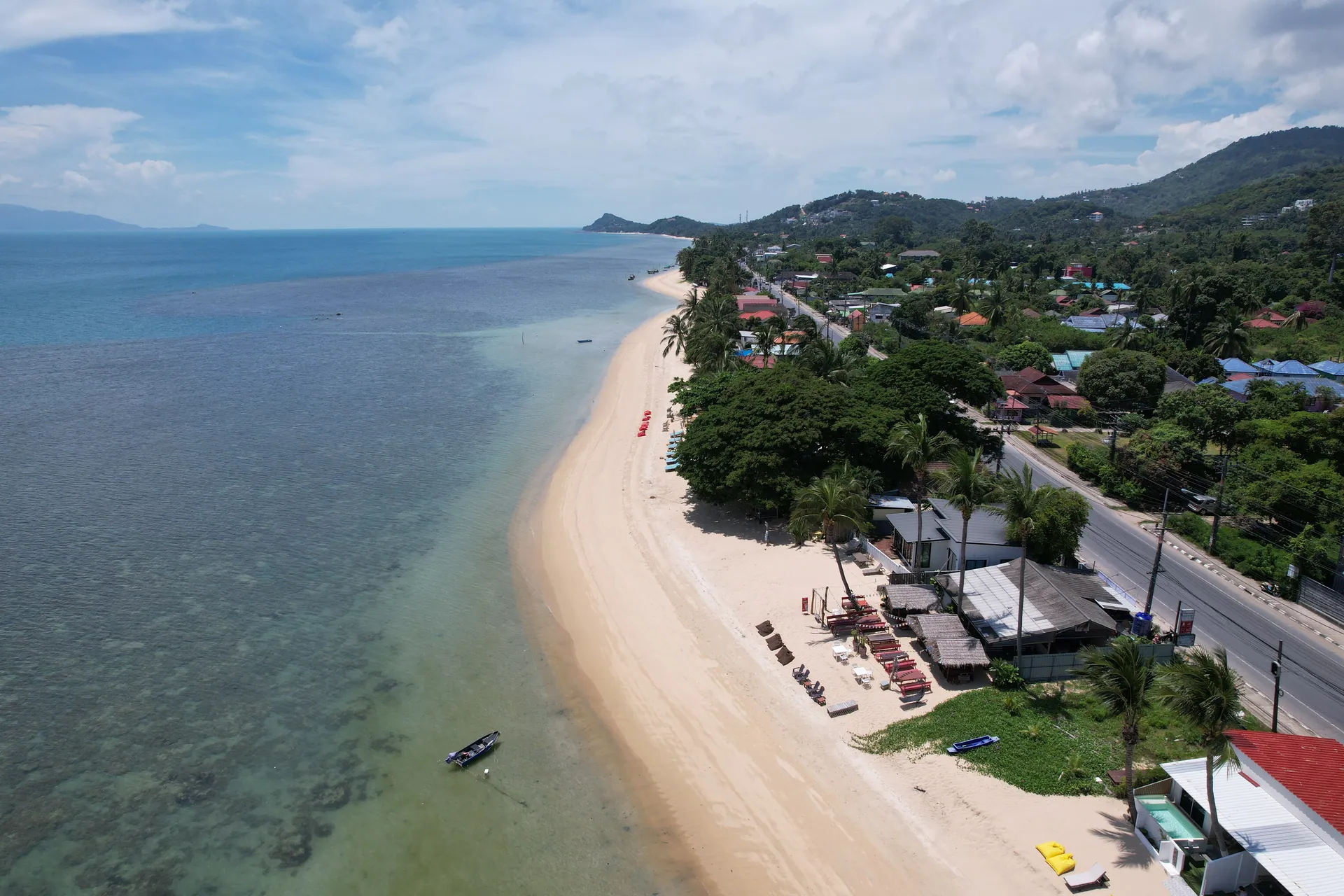 Aerial view of the long sandy beach and clear shallow water along the coast, with green hills behind