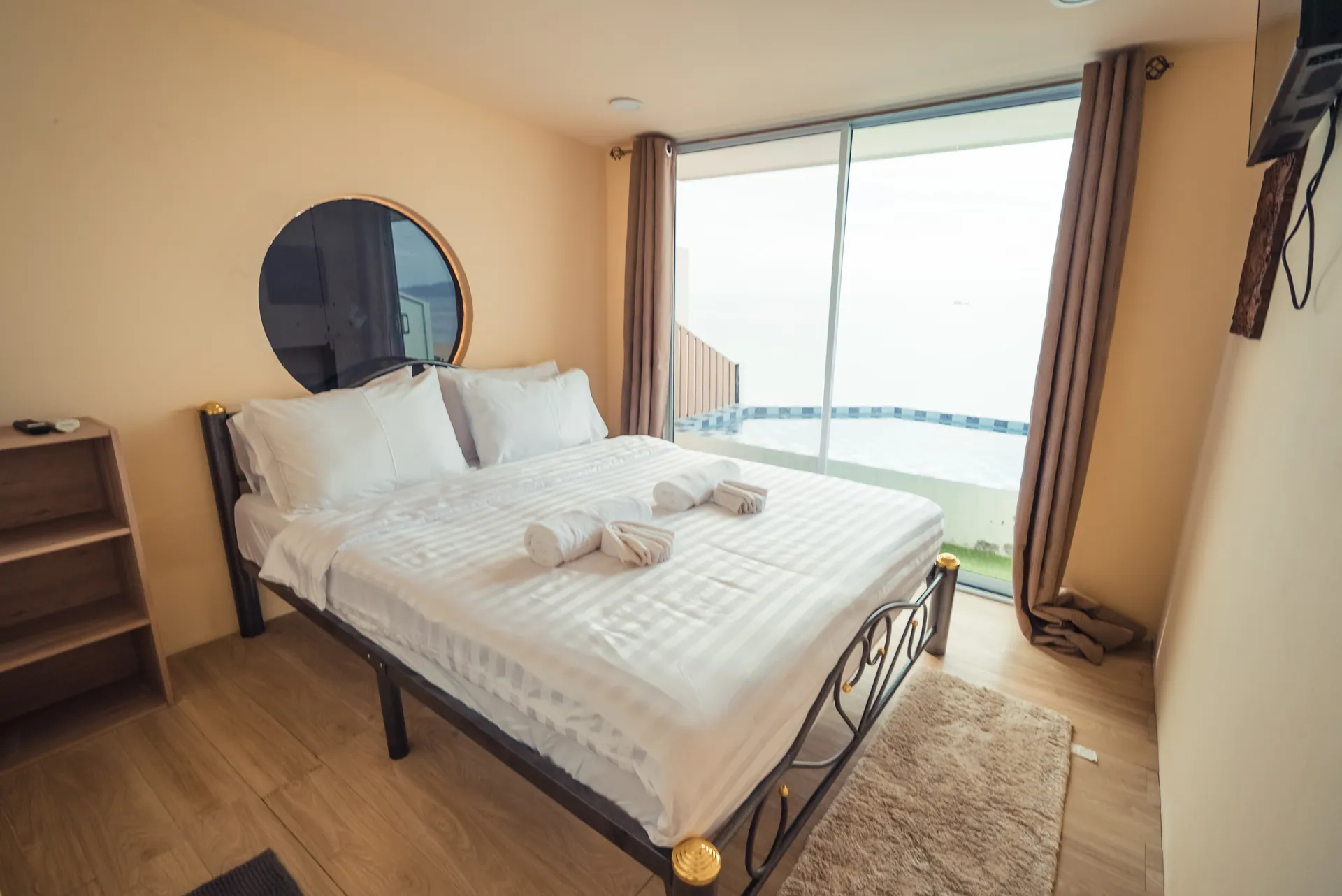 Bedroom with a black metal-framed double bed, a round porthole window and floor-to-ceiling glass facing the sea