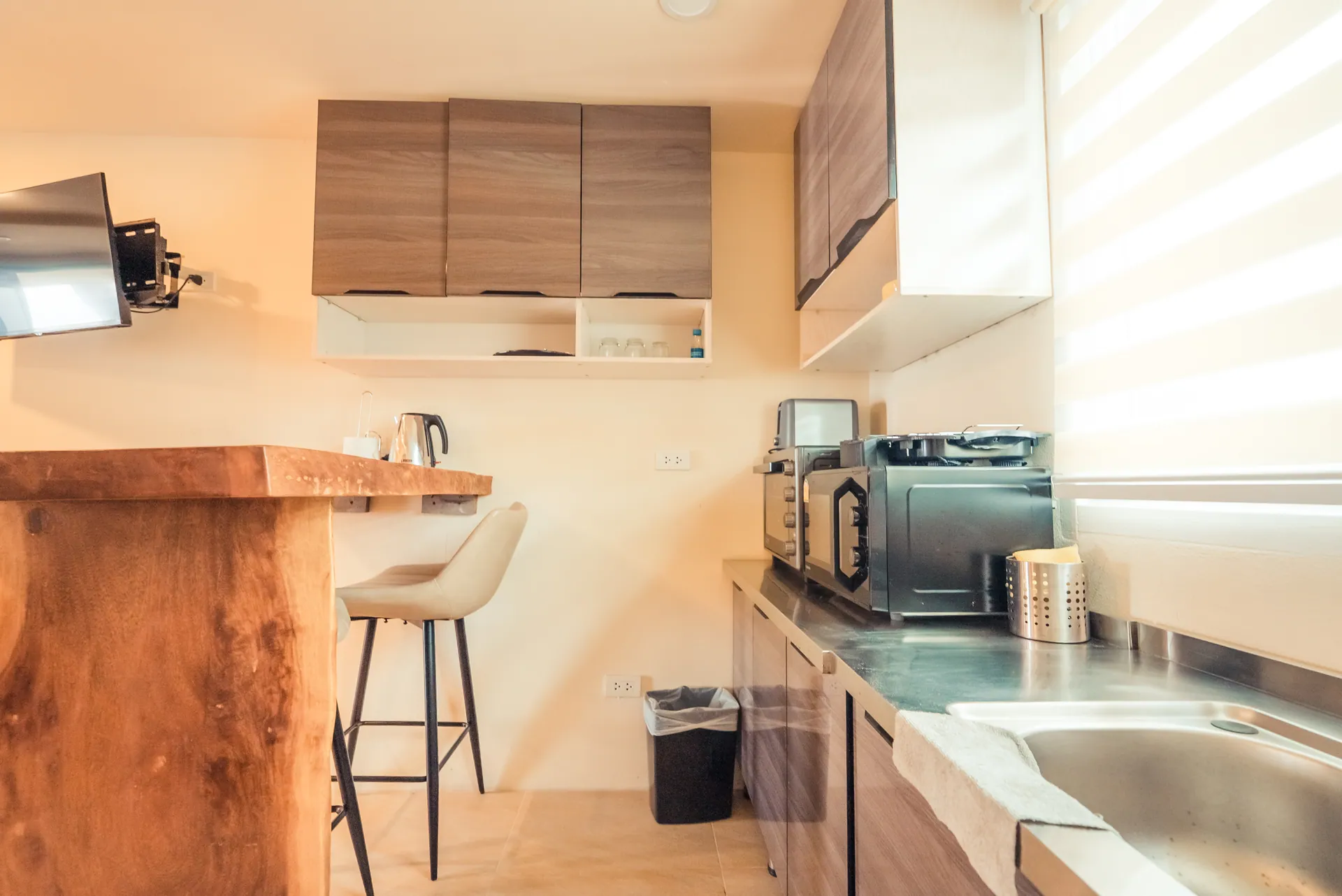 Kitchenette with a live-edge timber breakfast bar, a high stool, a microwave, a kettle and a stainless-steel sink
