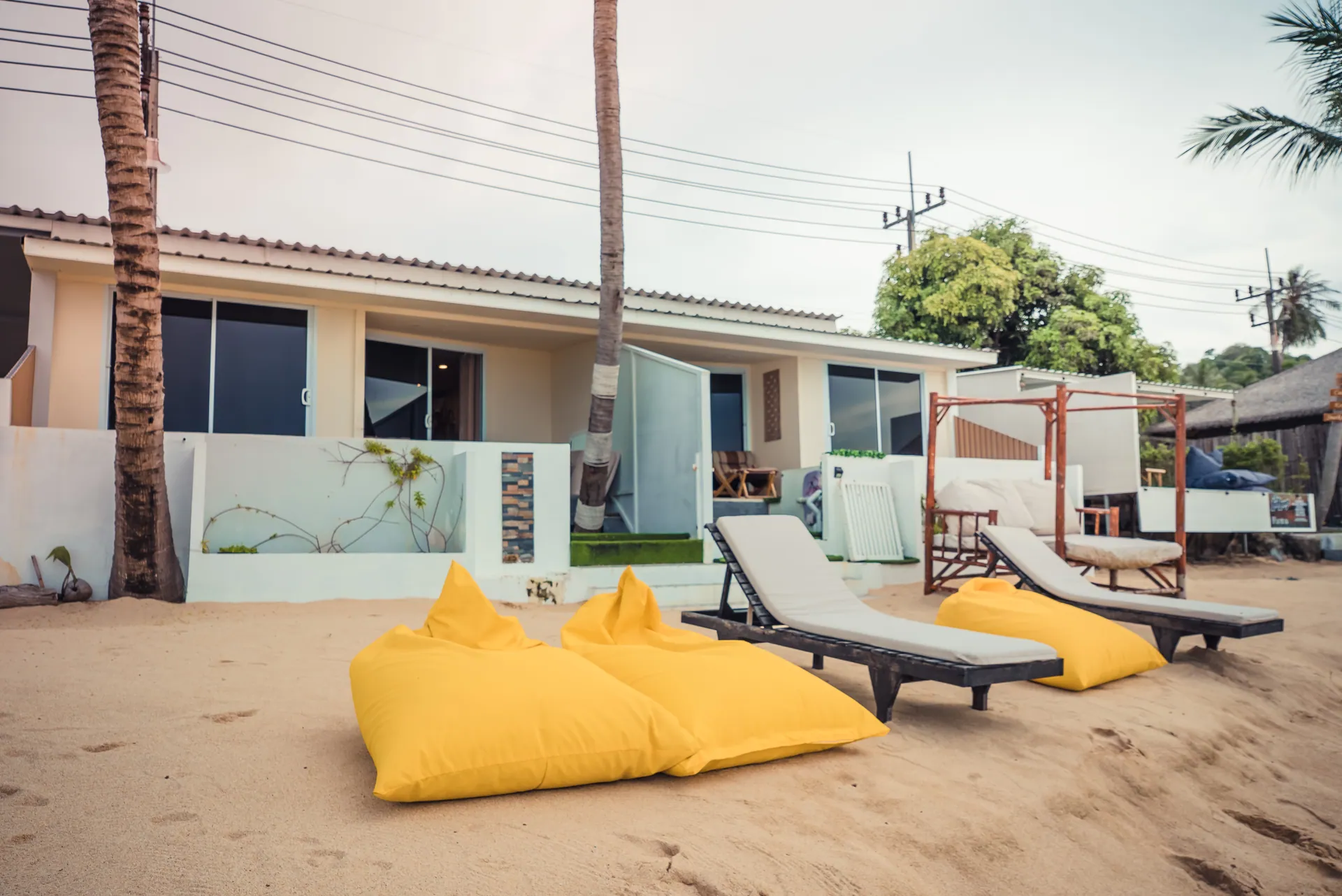 Single-storey villa facing the beach, with loungers, bean bags and a timber daybed on the sand in front