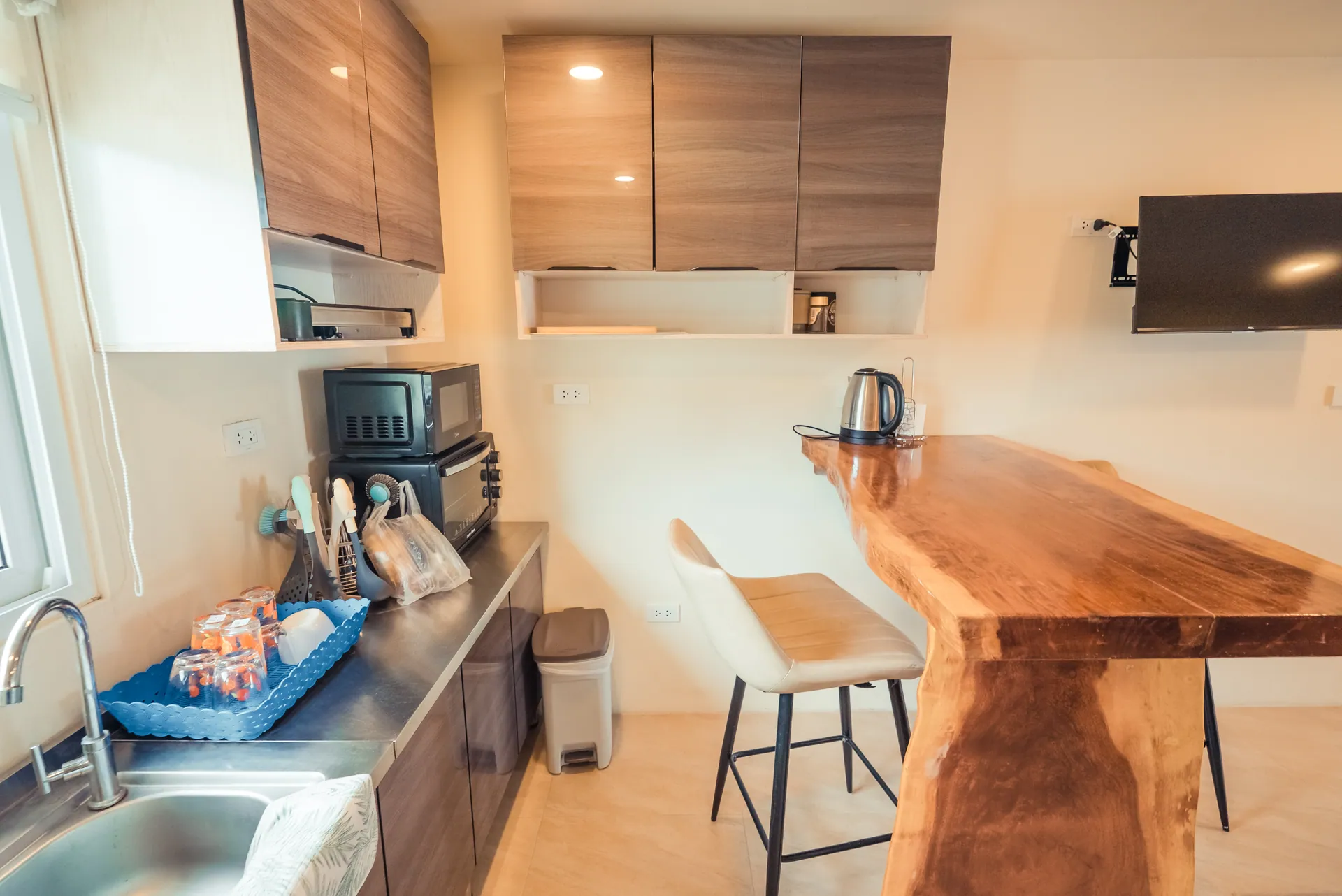 Second kitchenette with timber cabinets, a live-edge breakfast bar, high stools and a wall-mounted television