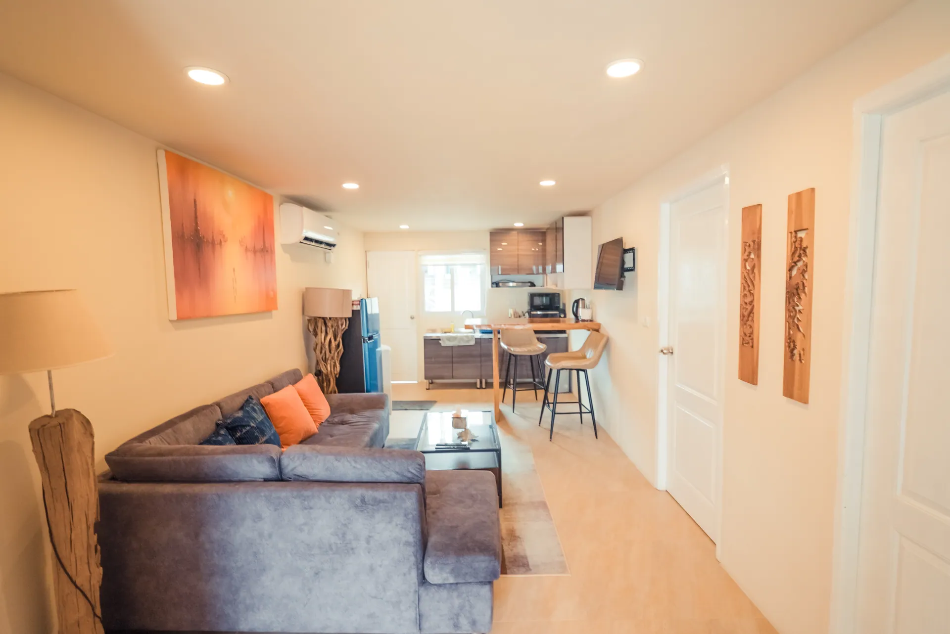 Second living room with a corner sofa, an abstract orange painting and a kitchenette at the far end