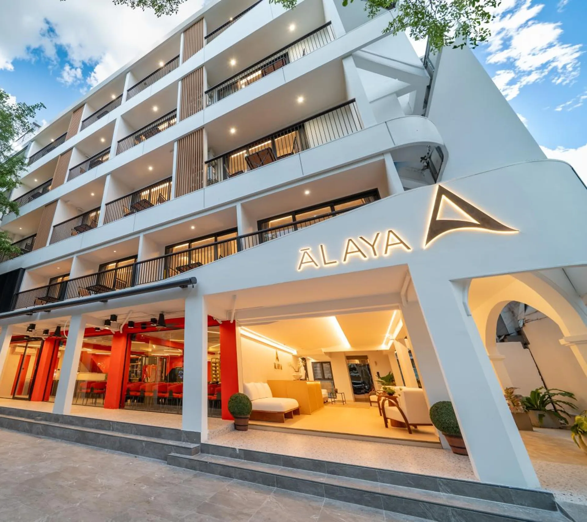 The hotel with its lit Alaya sign above the open lobby, and balconies on the floors above