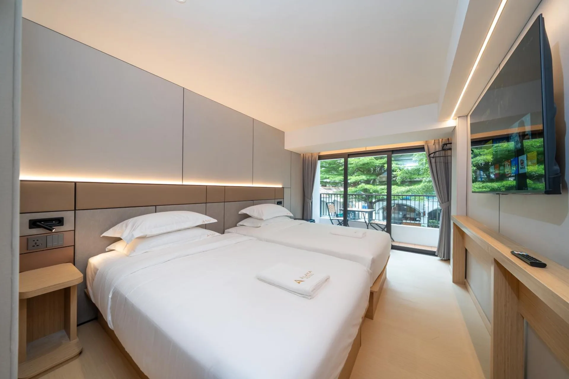 Two single beds and a wall-mounted TV, with glass doors to the balcony
