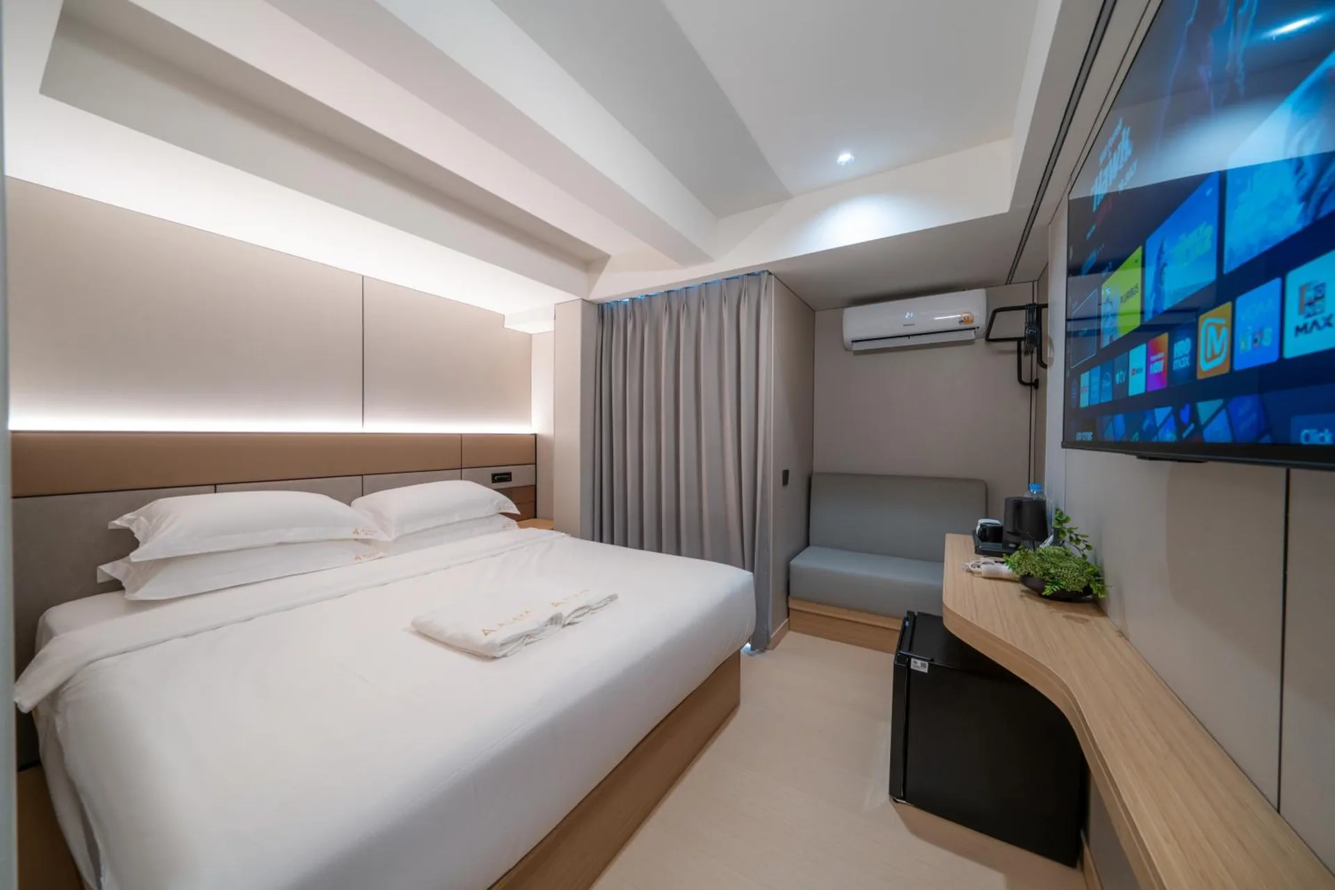 Queen bed with white linen, a wall-mounted TV and a curved timber desk